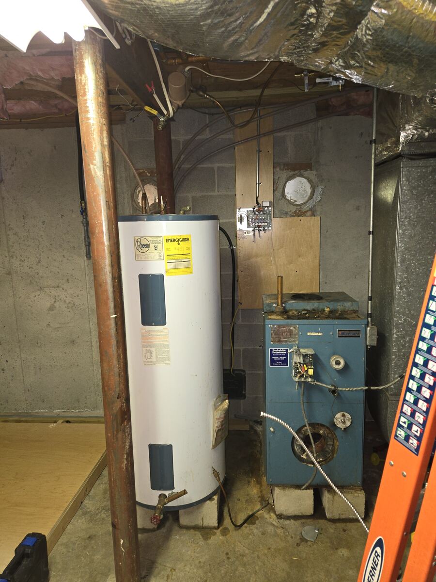Basement with a tall electric water heater standing next to an old oil boiler